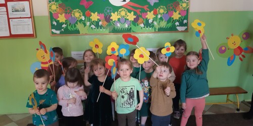 Dzieci stoja i trzymają własnoręcznie wykonane kwiaty.